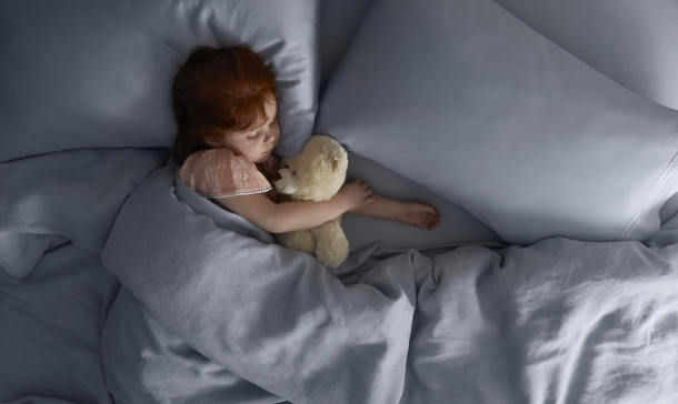 Red haired girl sleeping with a tan teddy bear.